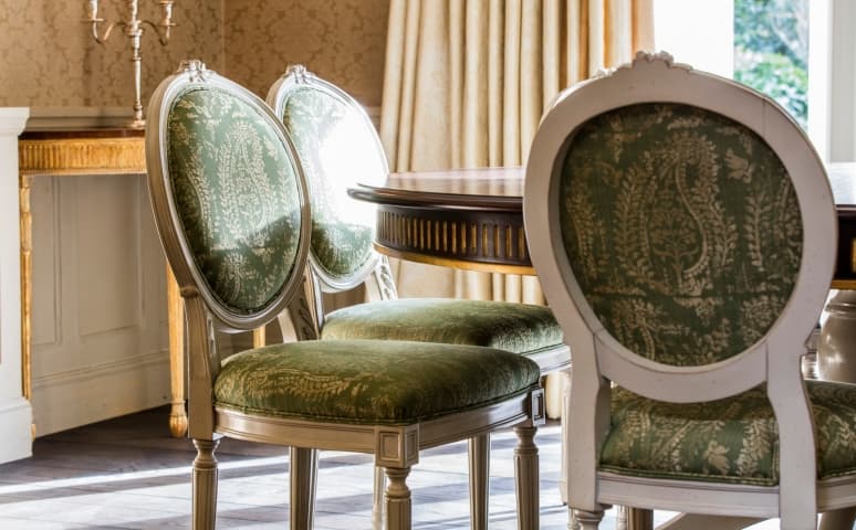 French dining chairs in green upholstery around a polished wood table
